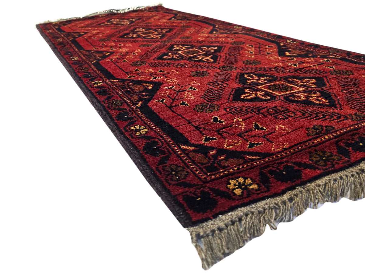Red patterned runner rug with central medallions and fringed bottom edge