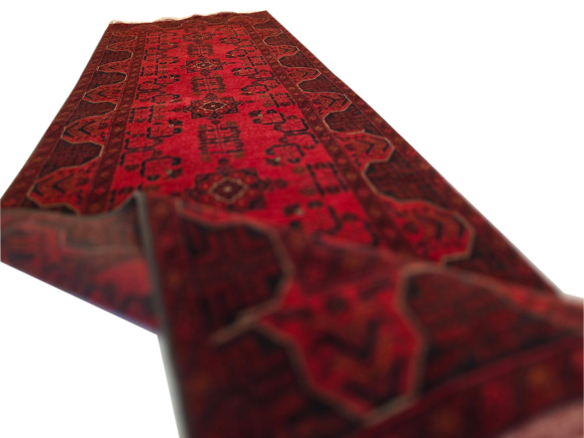 Red patterned runner rug with dark medallion motifs and tan fringe edge
