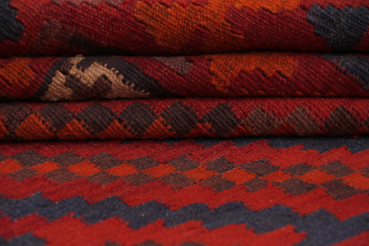Red kilim rug with dark zigzag and diamond geometric pattern, folded close-up.