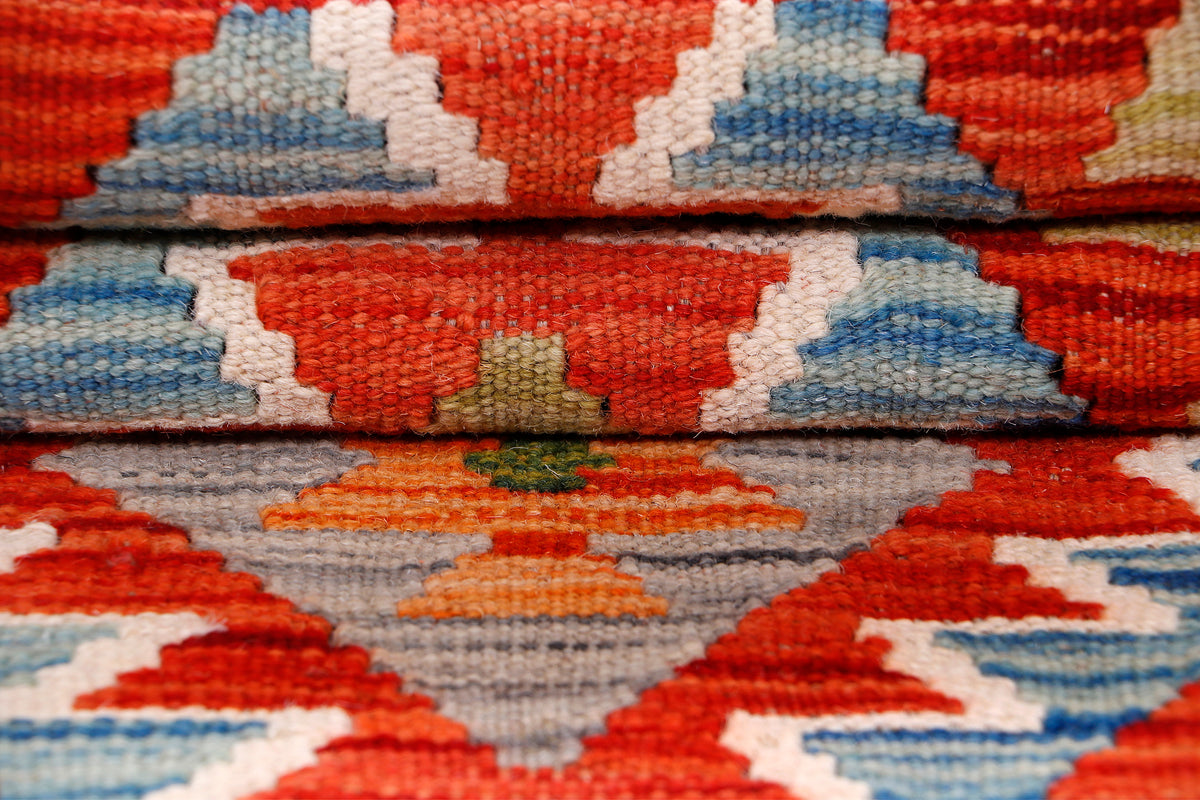 Kilim rug close-up of layered geometric pattern in red, gray, blue, and cream.