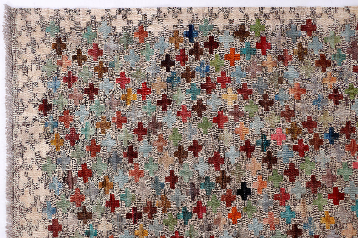 Beige kilim rug close-up with scattered multicolor cross shapes and mottled texture.