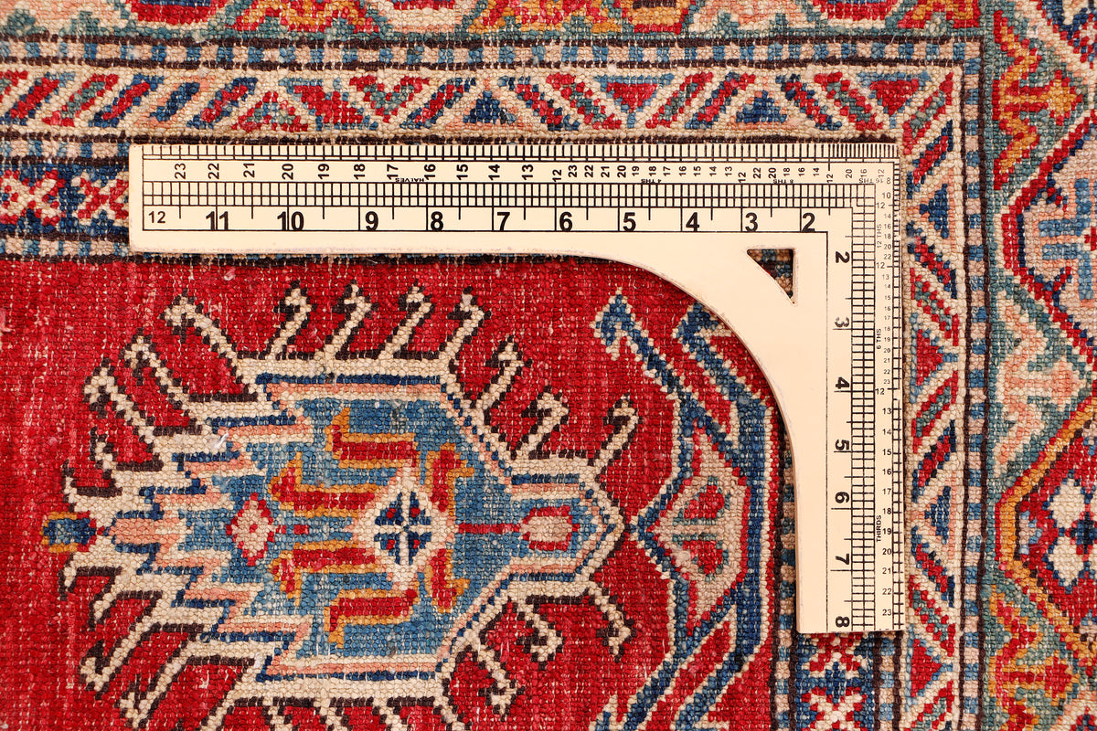 Red Kazak rug corner with ruler measuring tape across the patterned surface