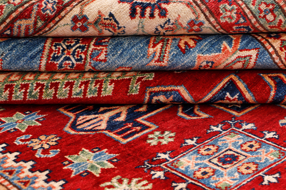 Folded Kazak rug with red, blue, and cream geometric patterns stacked in layers