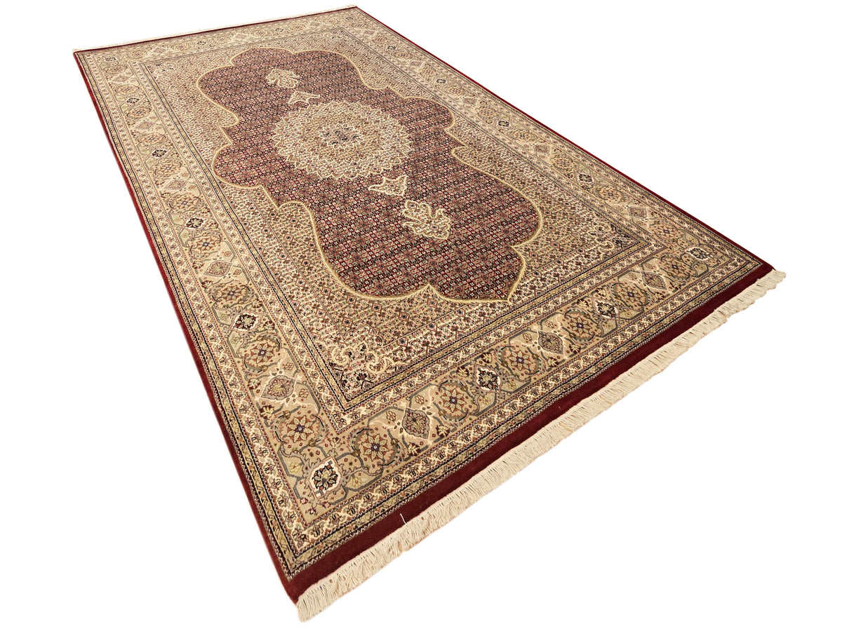 Patterned area rug with dark red floral medallion and cream fringe along side