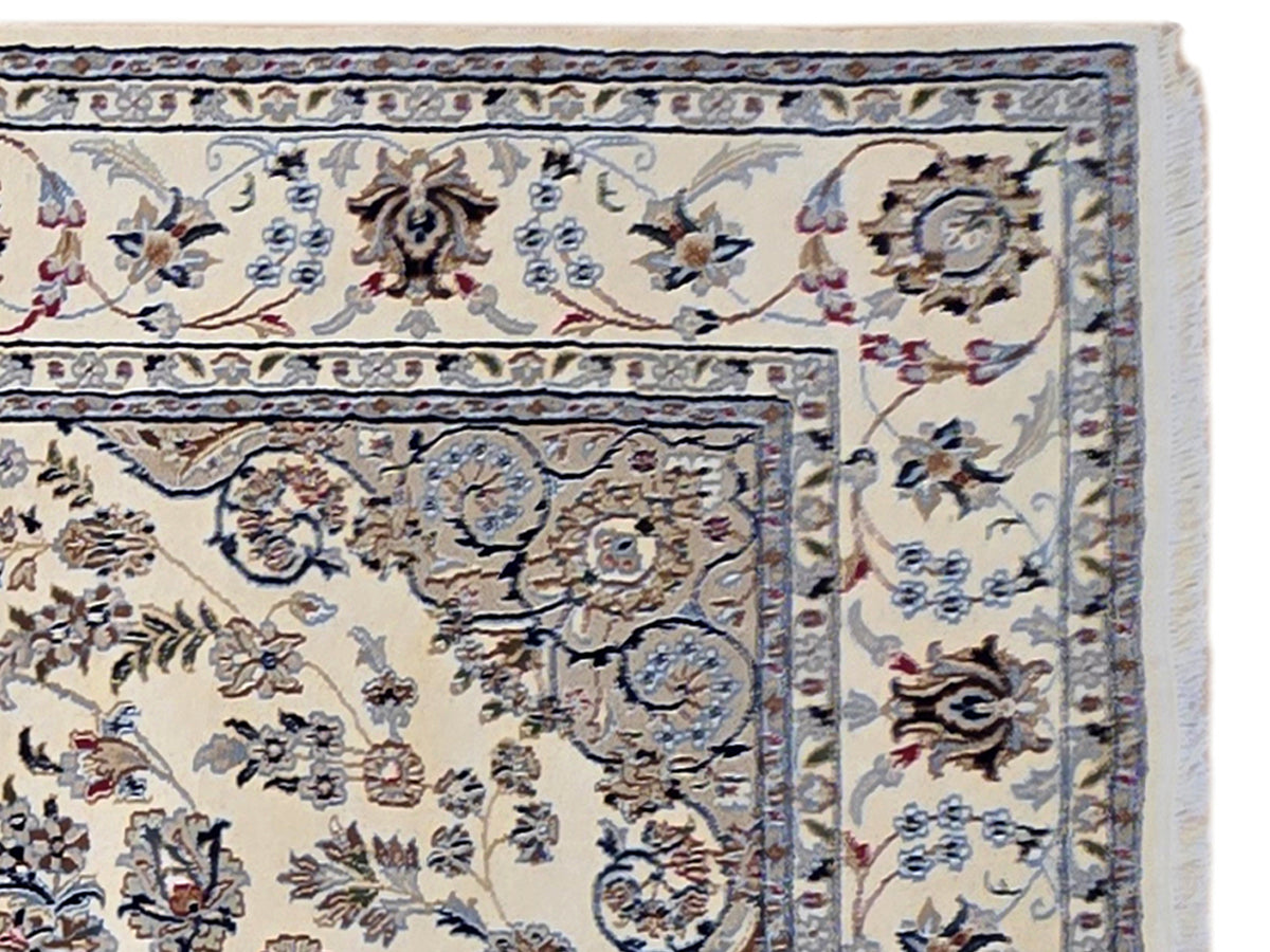 Close-up of ivory rug border with blue scrollwork and floral motifs, detailed edge trim.