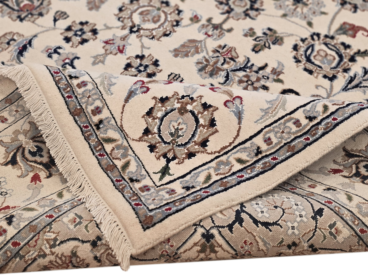 Close-up of ivory rug with navy and rust floral patterns, layered border, fringed corner.