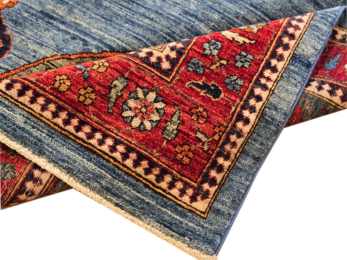 Close-up of rug corner with red floral motifs on blue background and fringe edge.