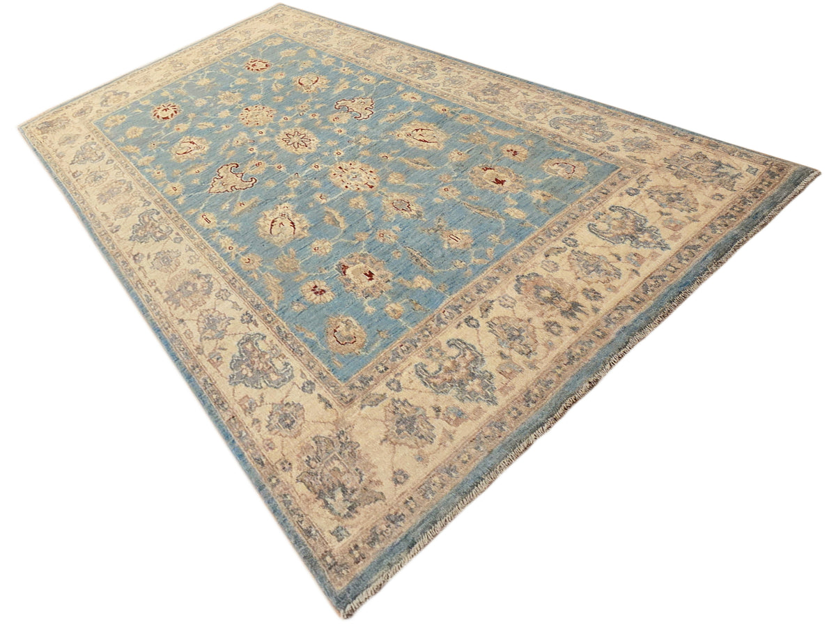 Diagonal view of light blue and beige ornate area rug with decorative border