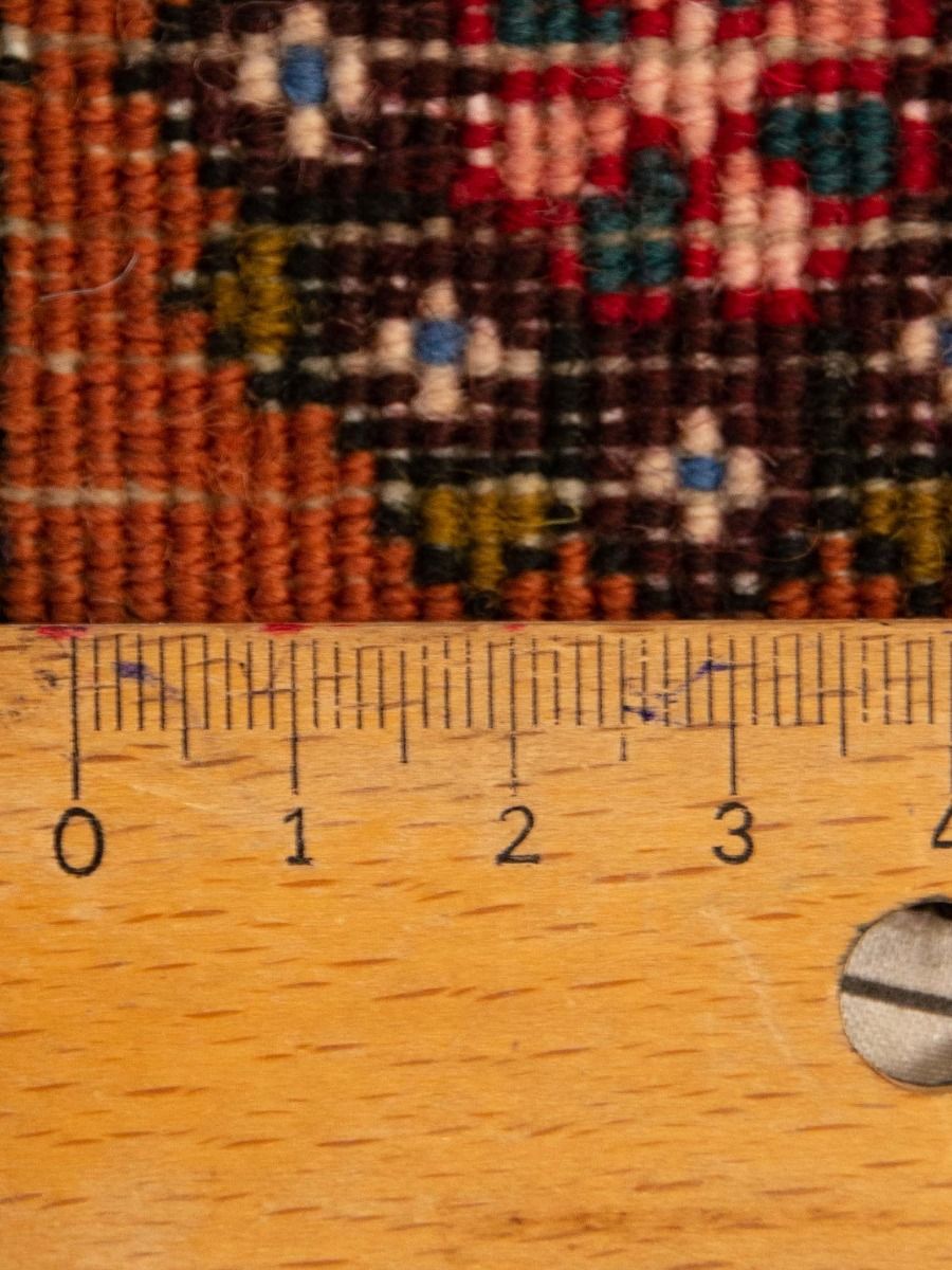 Close-up of Persian-style rug weave with multi-color geometric pattern beside ruler