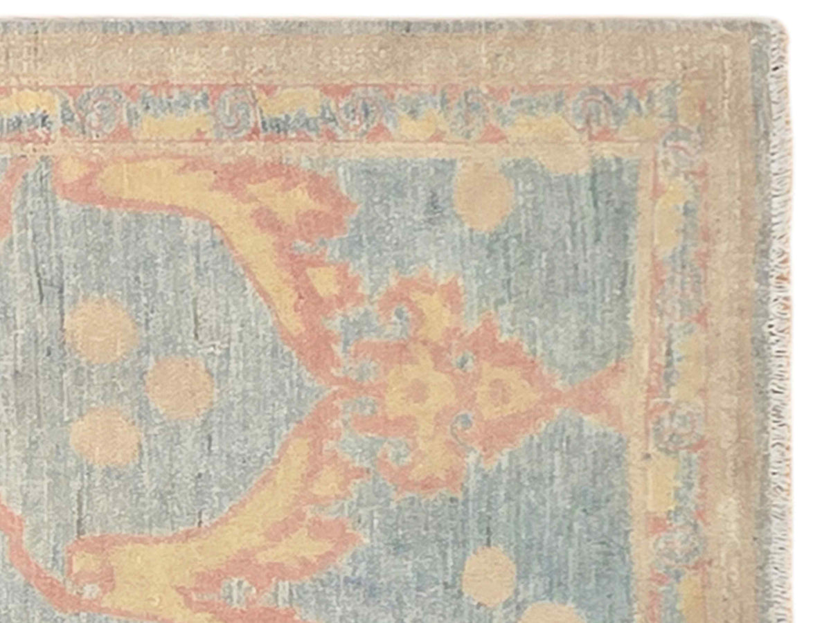 Close-up of light blue-gray rug with coral and beige ornate pattern and frayed edge