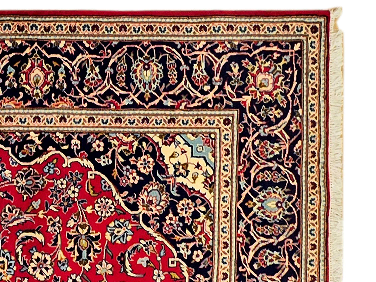 Kashan rug close-up, dark navy field with red floral motifs and cream edging