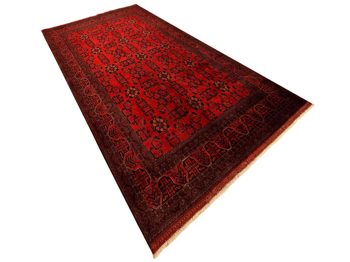 Dark red area rug with repeating geometric pattern and tan fringe border detail.