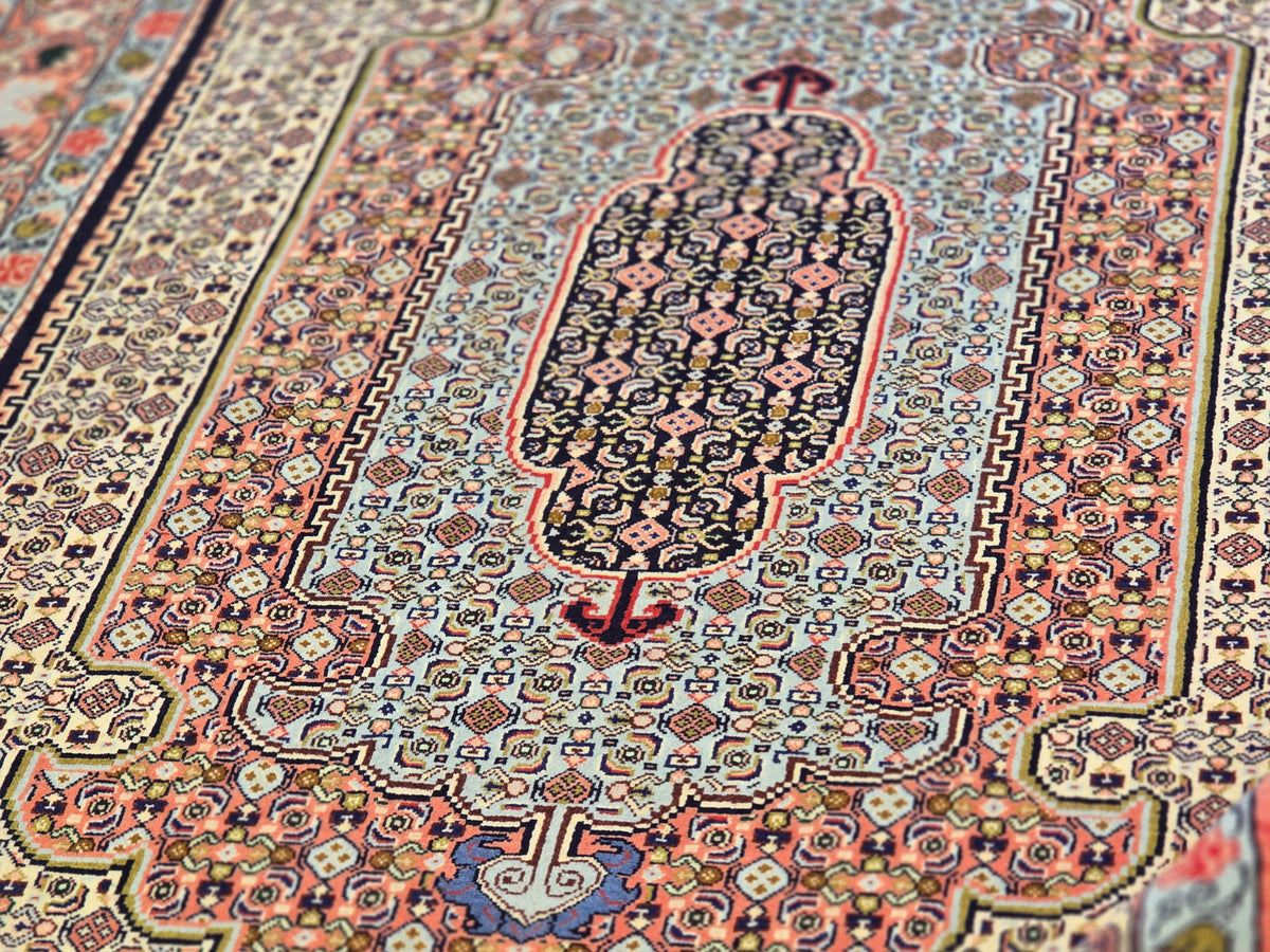 Detailed floral and geometric pattern on area rug in red, blue, cream, and black tones.