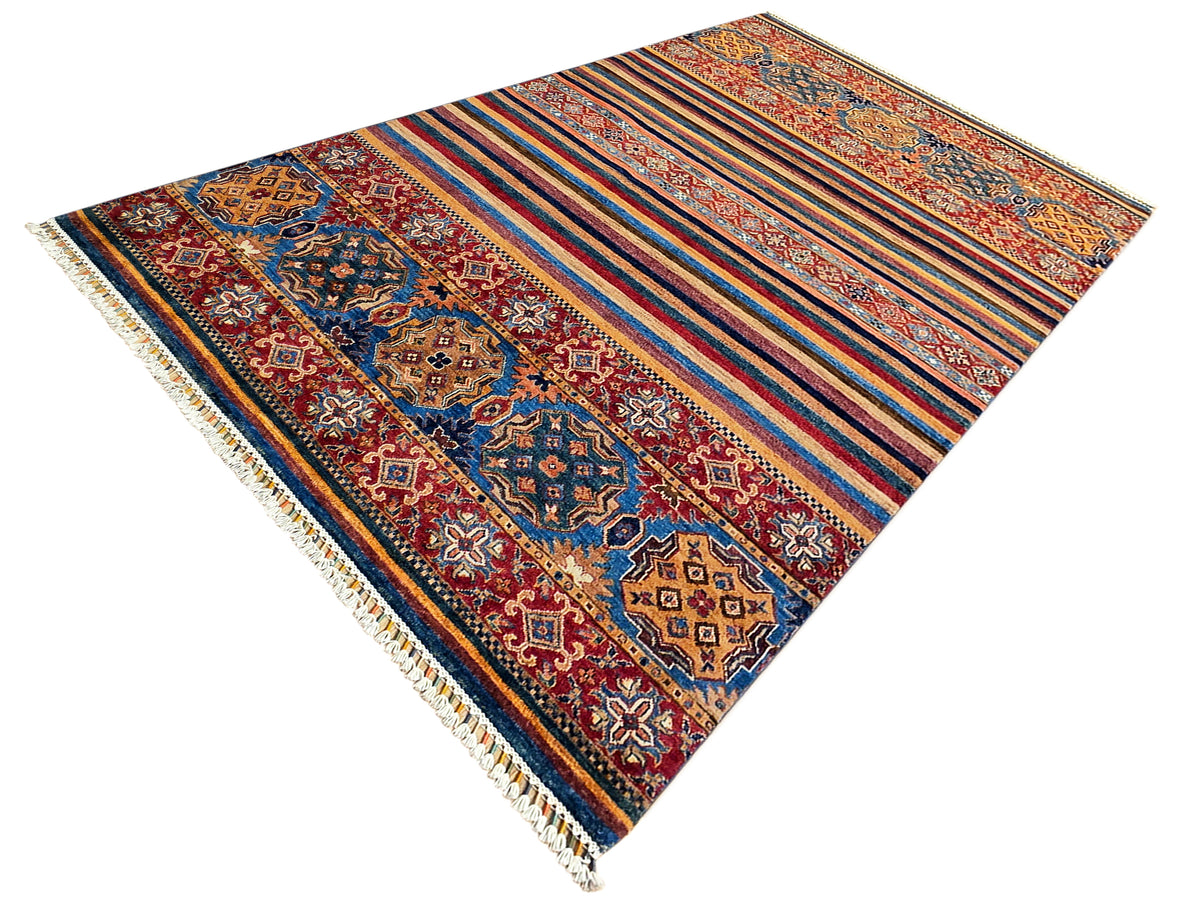 Corner view of multicolor woven rug with diamond motifs, stripes, and short fringe