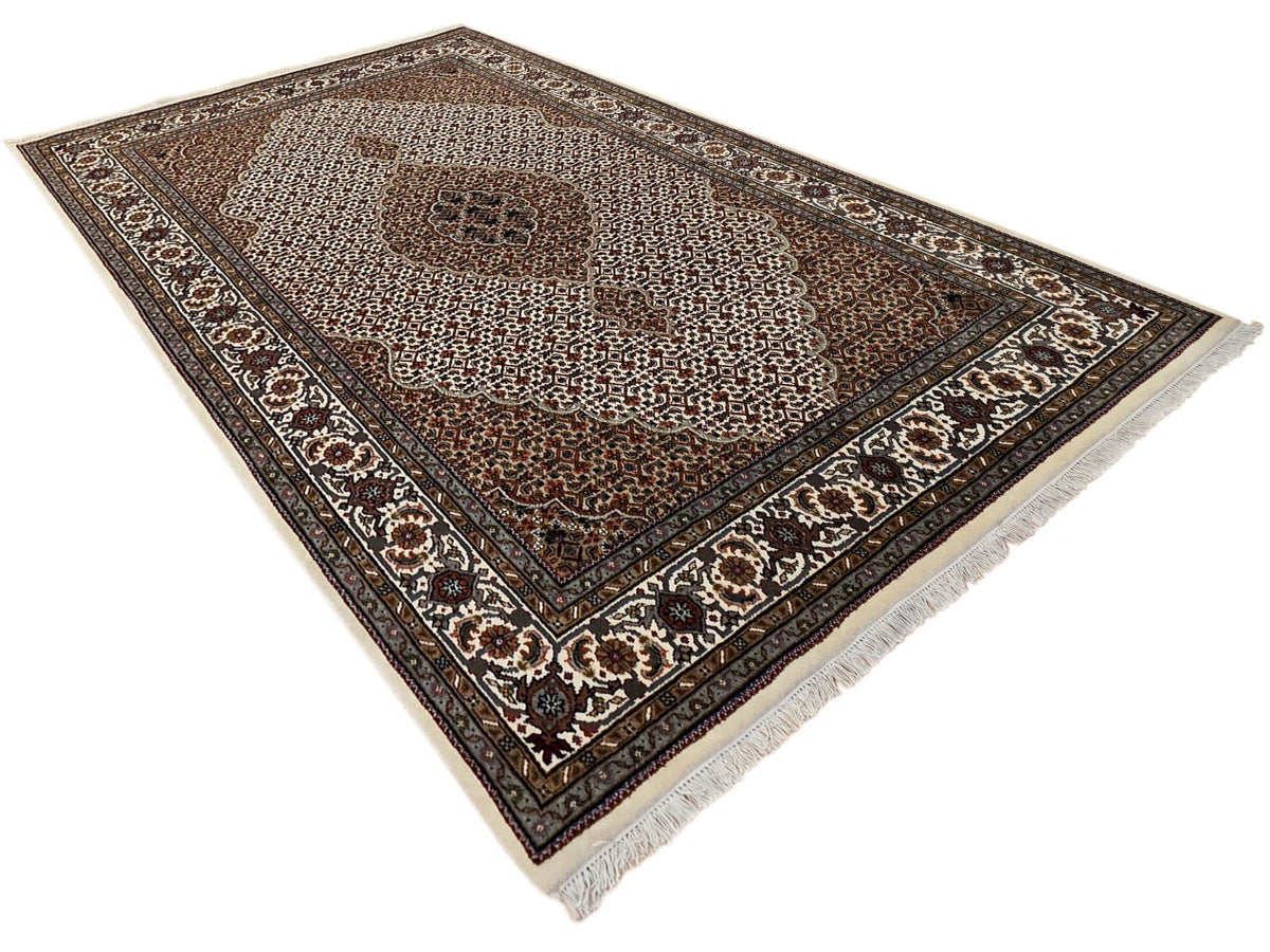 Folded oriental rug with brown lattice motifs, cream accents, dark blue border, fringed edge