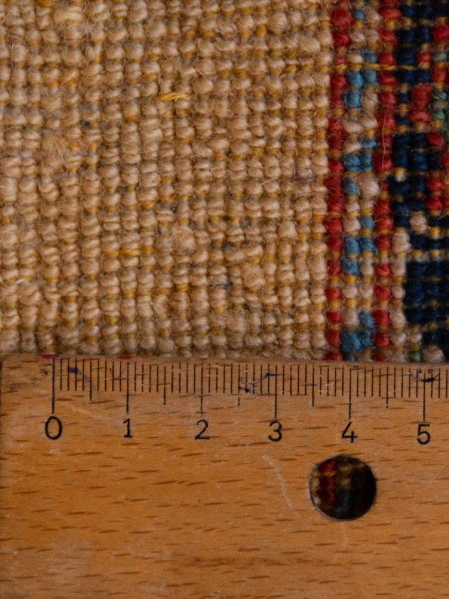 Rug texture close-up with tan fibers and multicolor woven edge; measuring tape on bottom