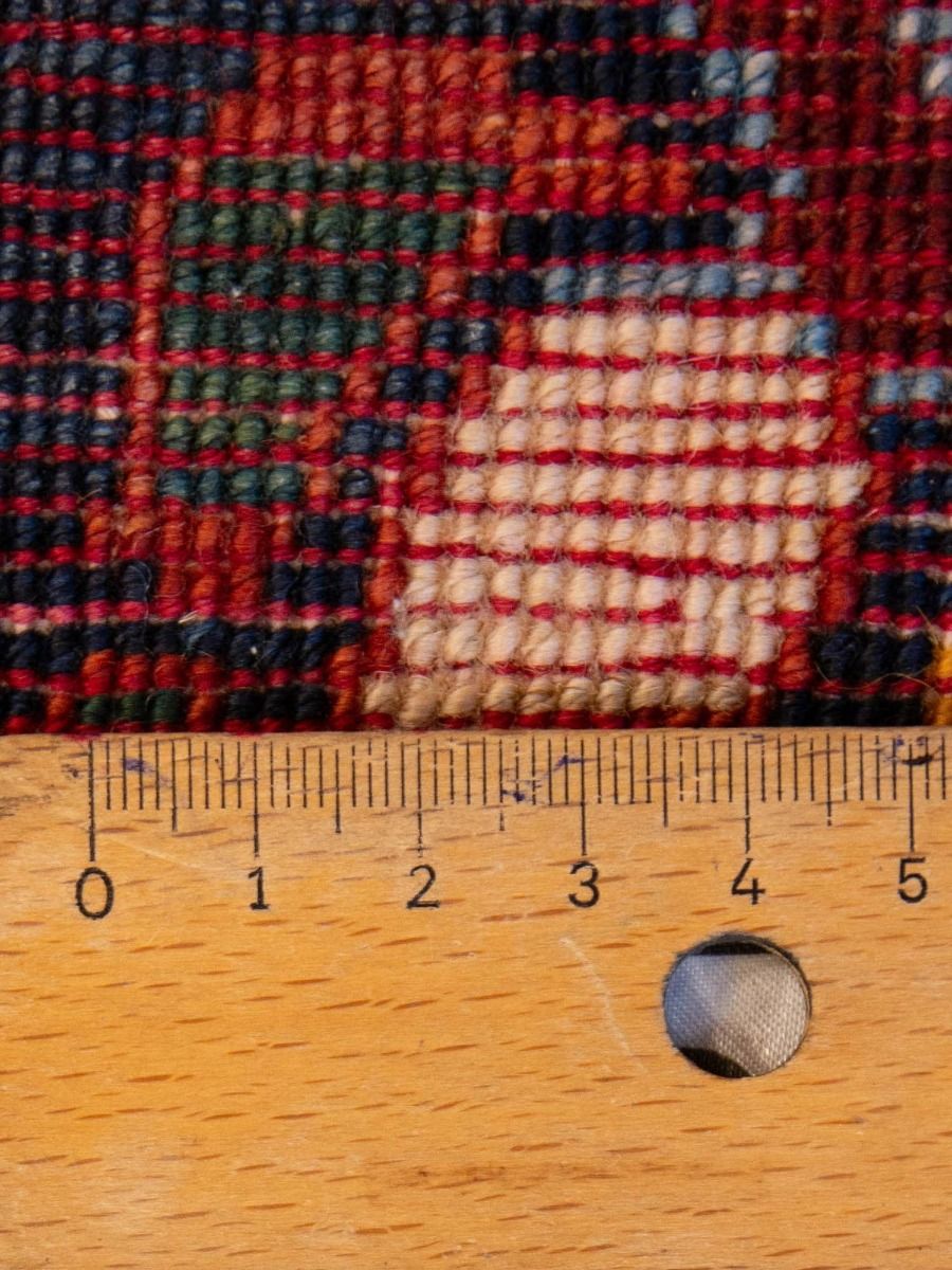 Rug close-up, multicolor woven texture in navy, rust, and cream with measuring ruler