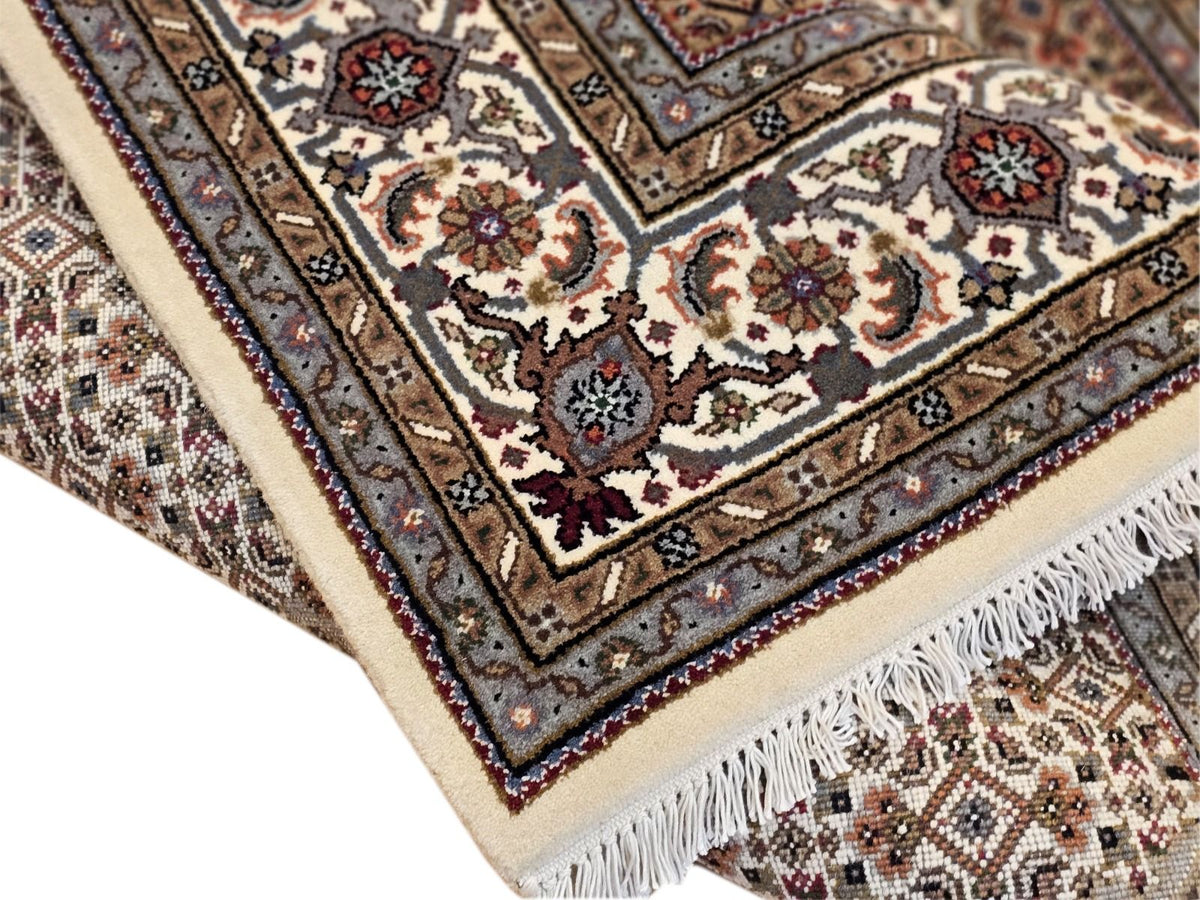 Oriental rug corner with cream field, ornate medallion, and dark border; visible fringe