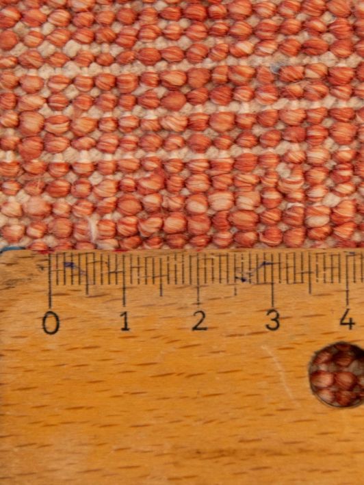 Close-up of orange textured rug pile with blue threads and ruler for scale.