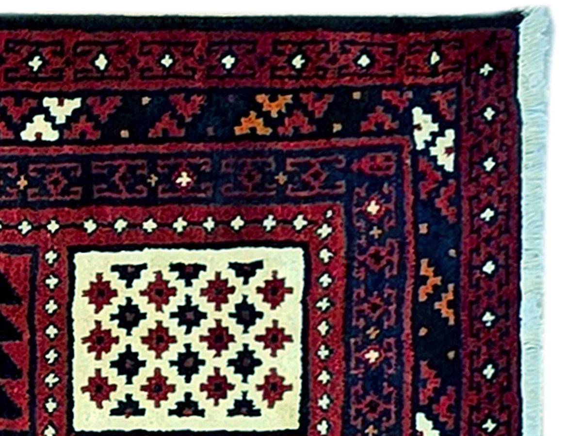 Close-up of Persian-style rug border with dark red field, cream and green motif clusters.