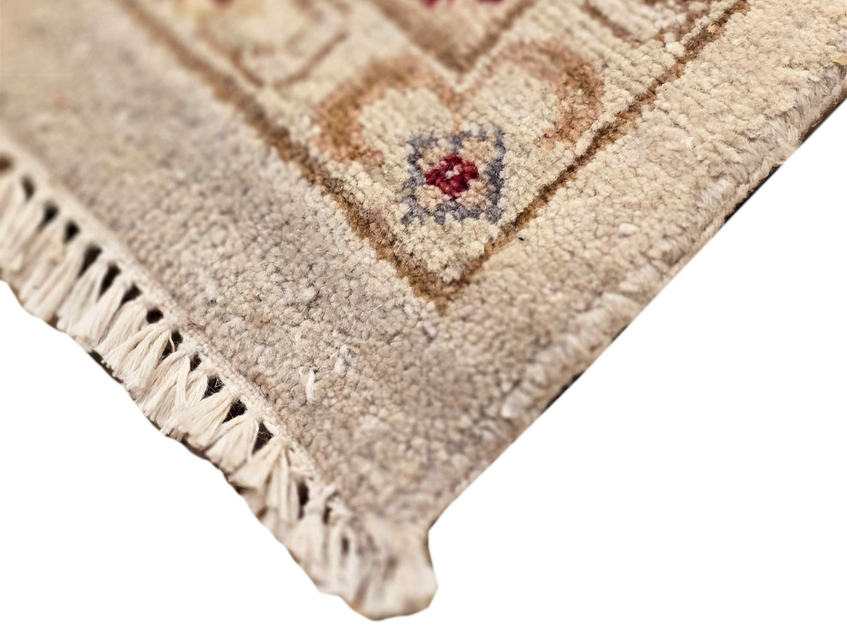 Close-up of rug corner with cream pile, burgundy-and-brown motif, short fringe edging