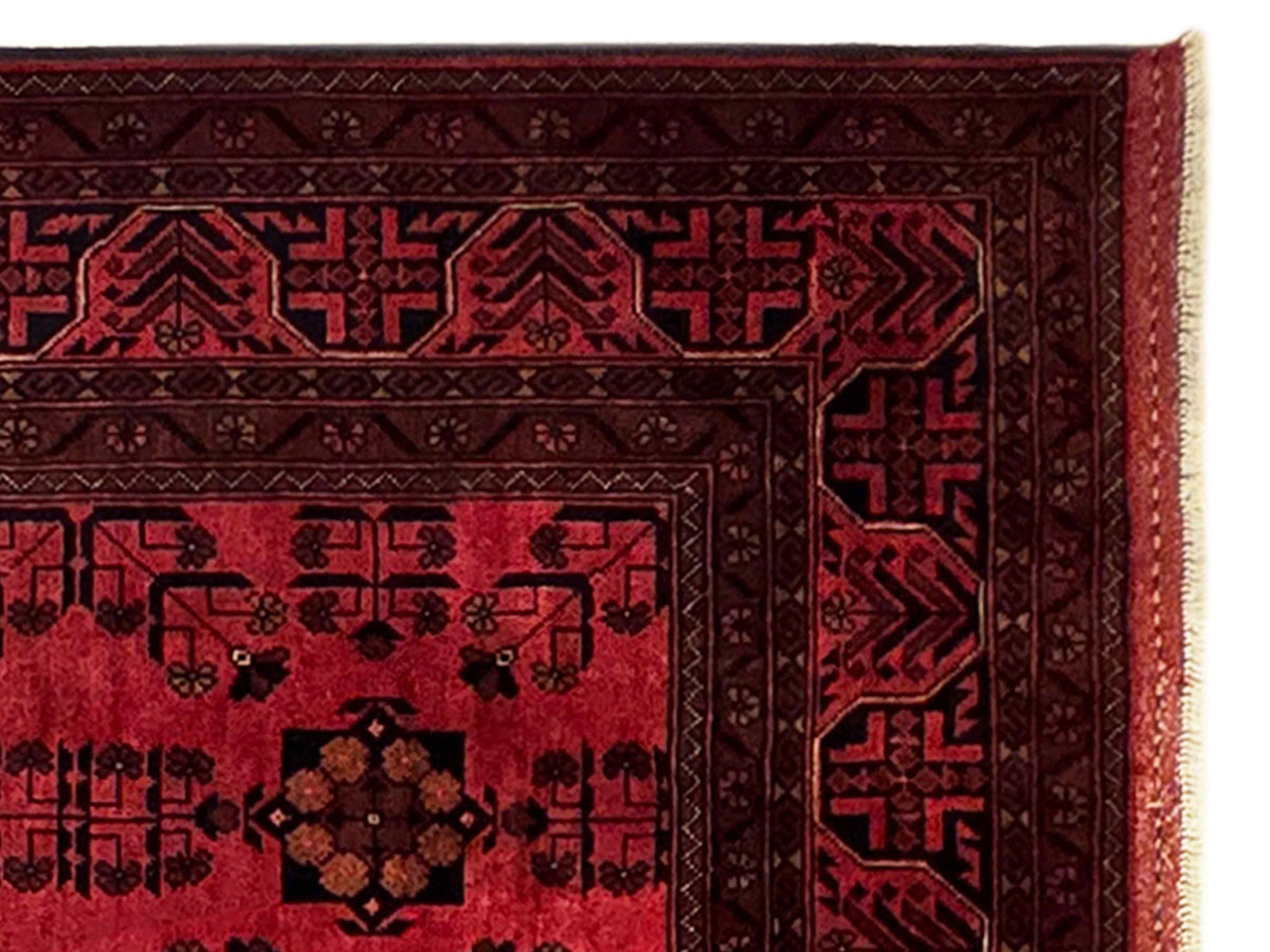 Close-up of red and dark rug border with geometric motifs and fringed edge.