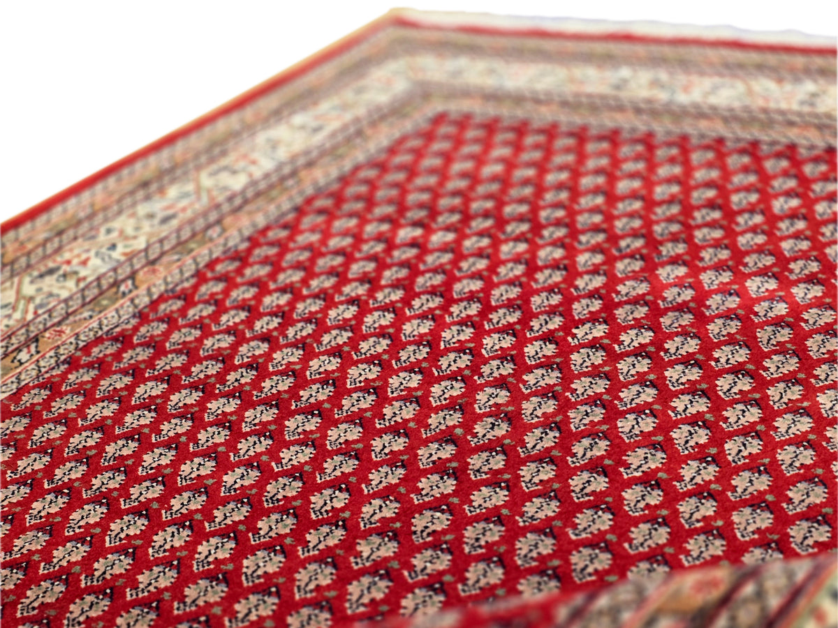 Red rug surface close-up with repeating diamond pattern and cream trim border.