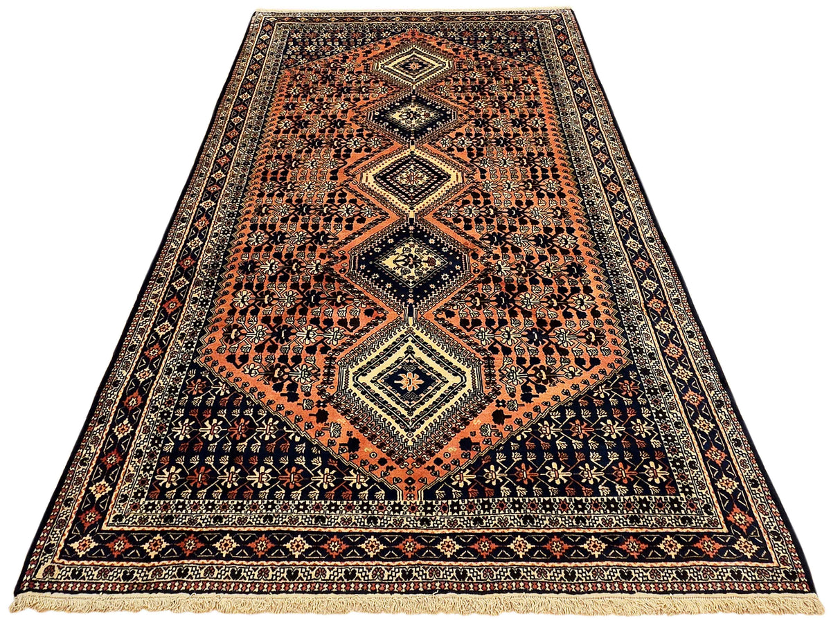 Orange and dark navy diamond medallion area rug with patterned border and cream fringe