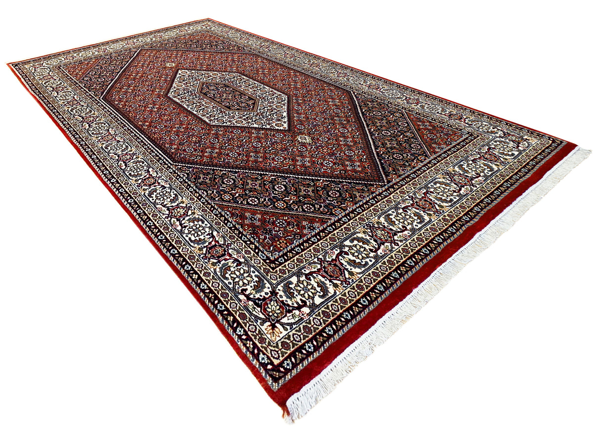 Red patterned area rug with central medallion, detailed border, and cream fringe
