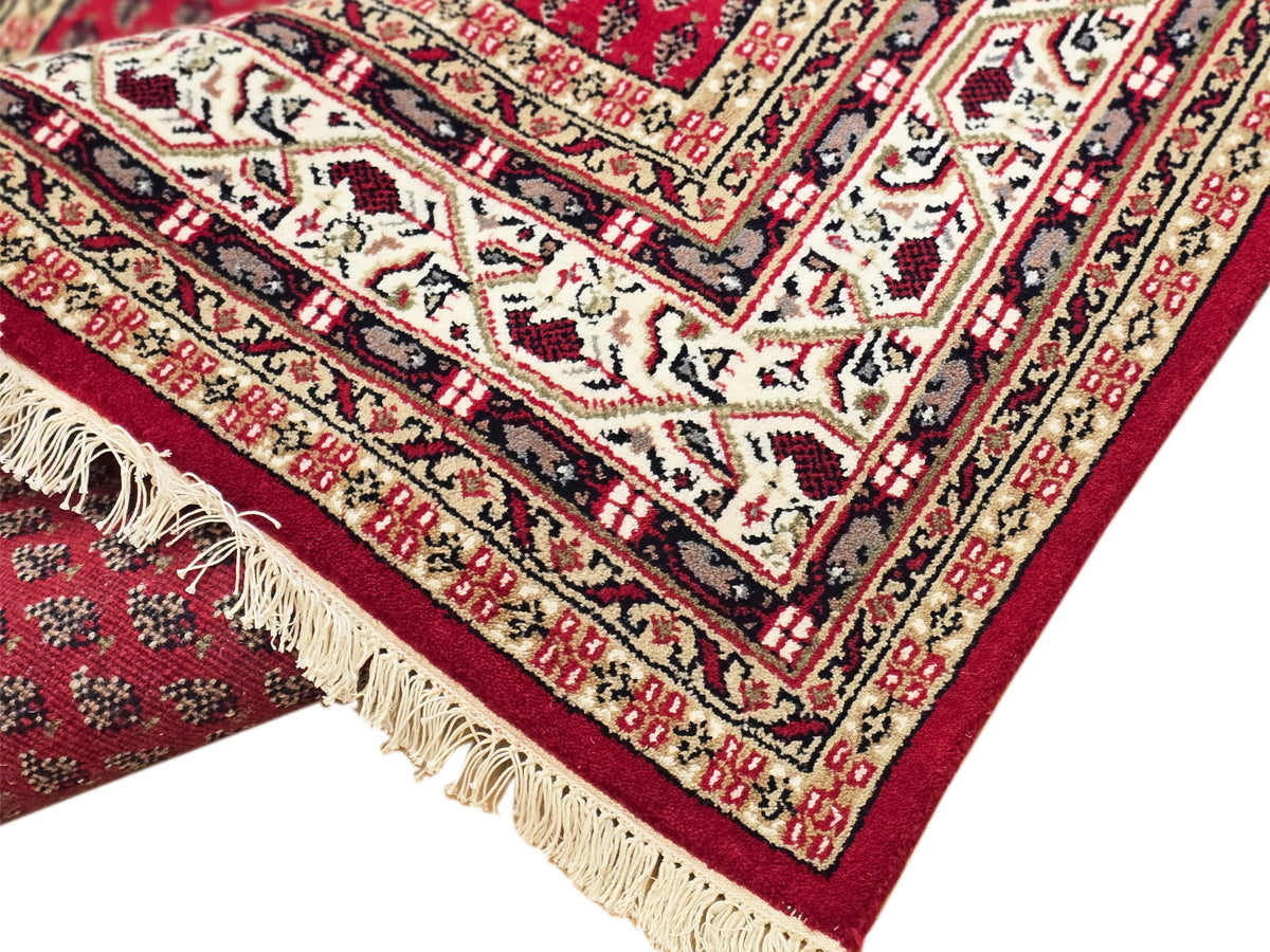 Close-up of red rug border with cream, black, and patterned motifs and cream fringe