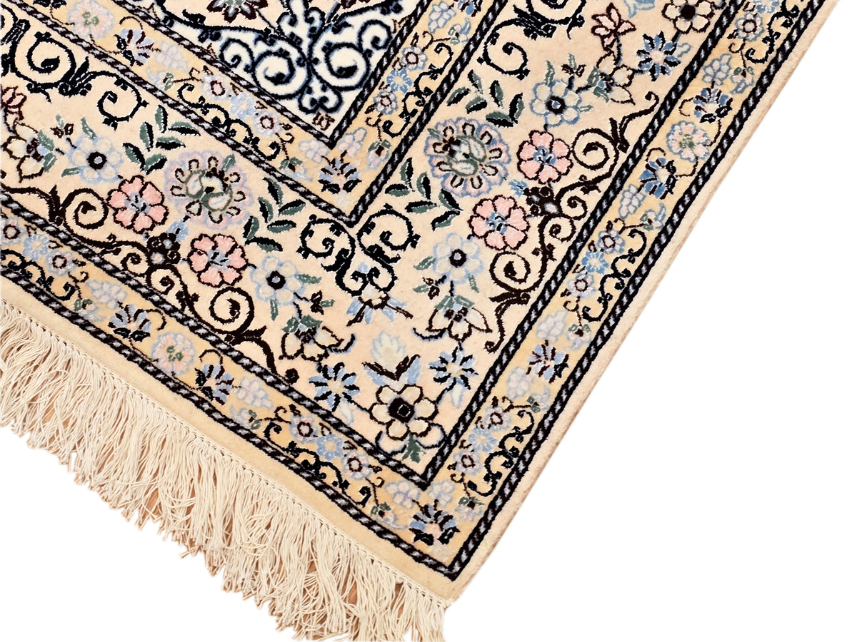Corner of cream area rug with blue border, floral motifs and long tassel fringe