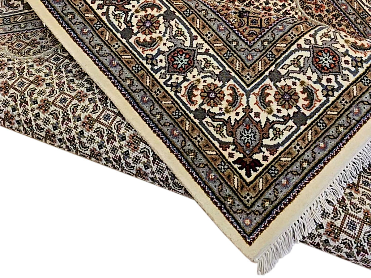 Rolled diagonal view of patterned area rug with fringed edge and cream-trim border.