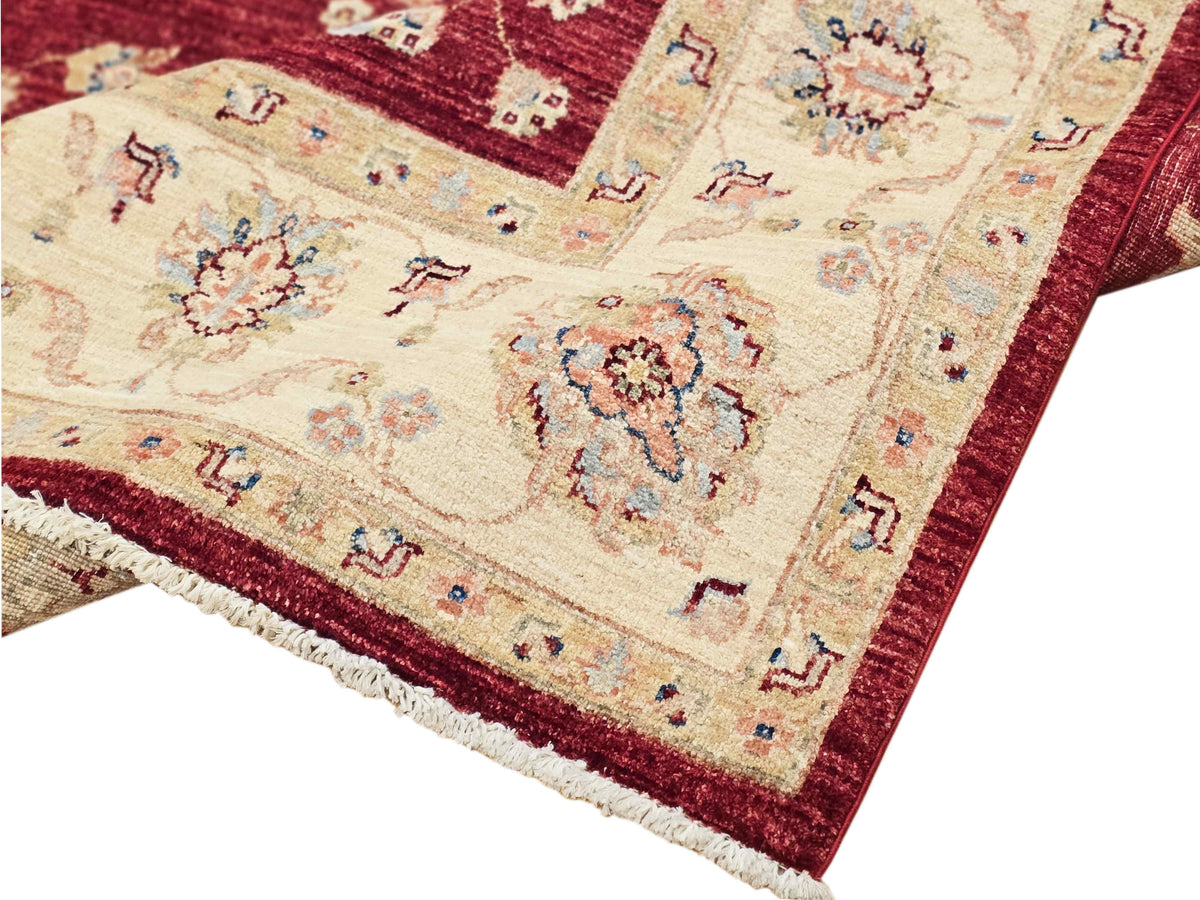 Corner close-up of red and cream rug with floral medallions and fringed edge