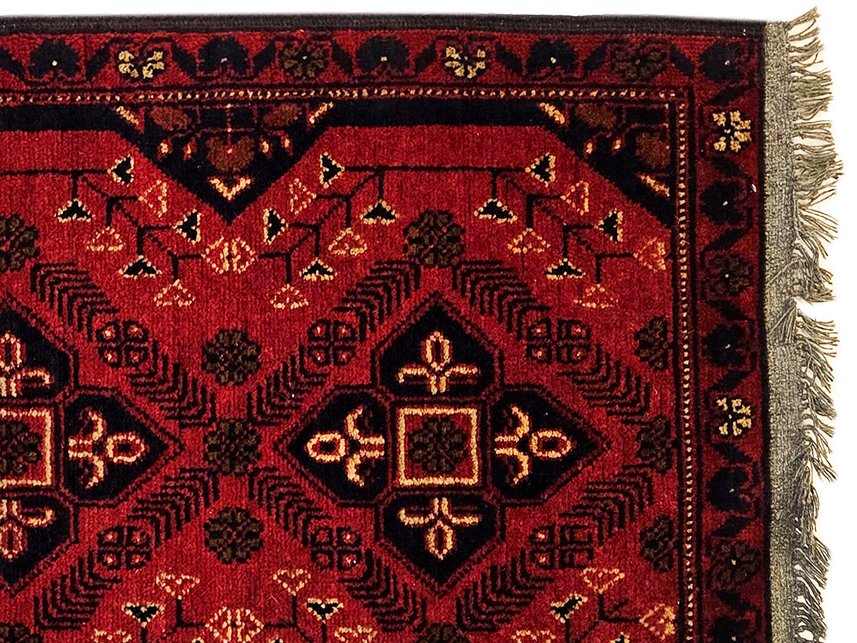 Close-up of red geometric rug pattern with dark borders and fringe at right edge