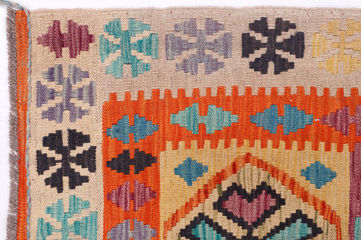 Kilim rug close-up with beige ground and orange, teal, purple geometric motifs