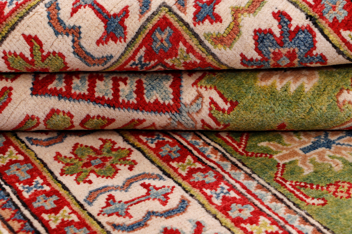 Green rug with folded edge showing red and cream floral geometric motifs