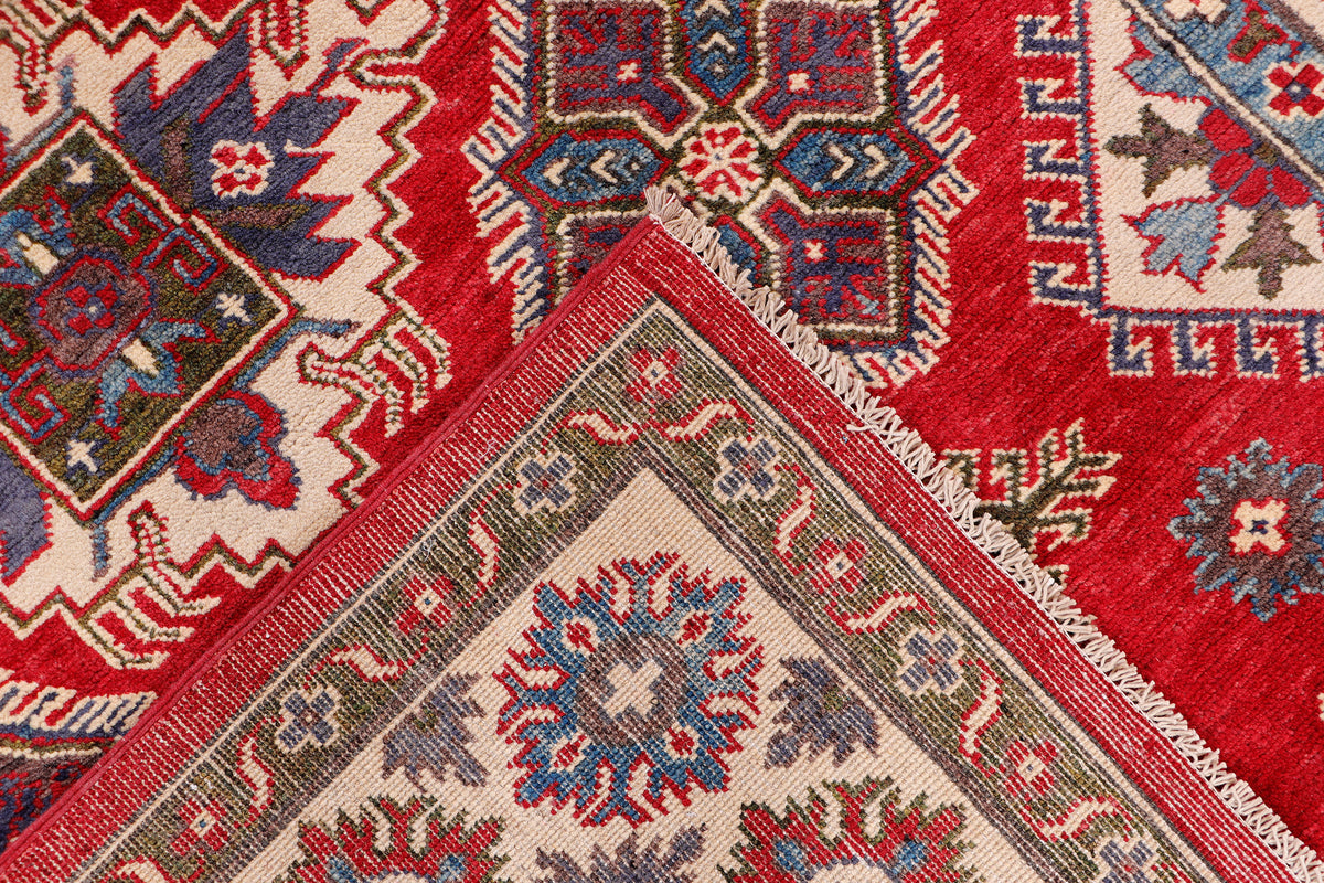 Red rug close-up with geometric motifs in blue, gray, cream, and white