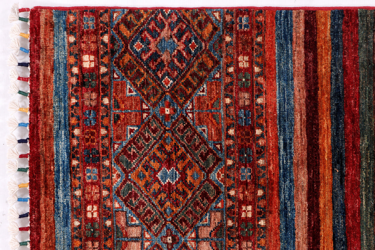 Red patterned area rug with blue and brown stripes and diamond motifs, fringed border