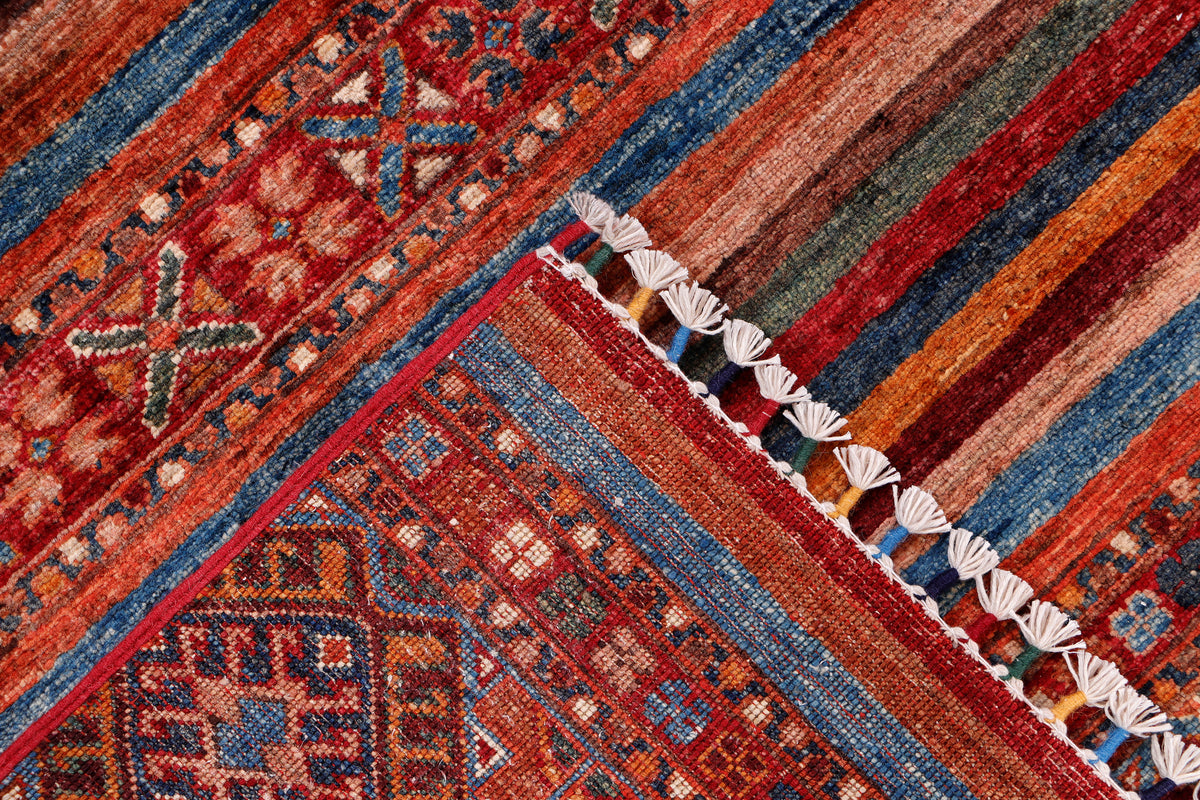 Corner of red rug with multicolor stripe bands, decorative motifs, and white fringe