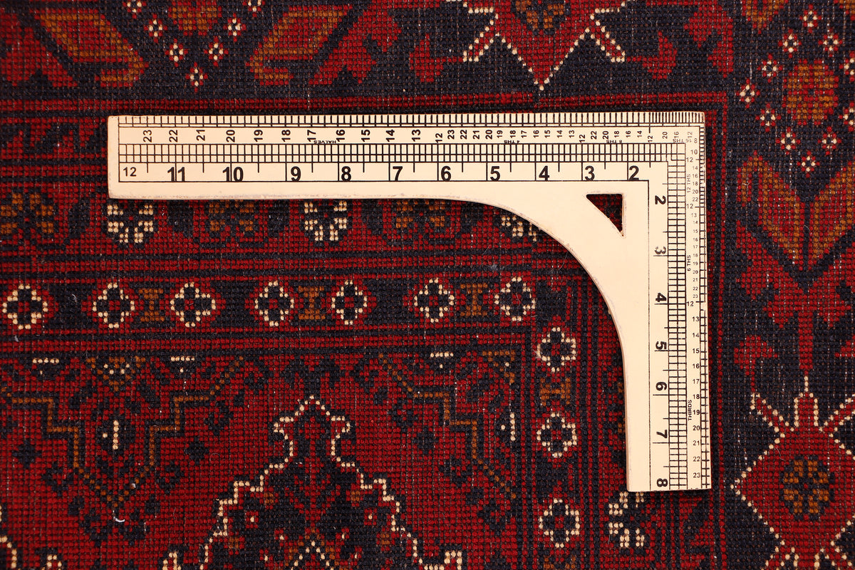 Red rug border with geometric motifs and measuring tape along the edge