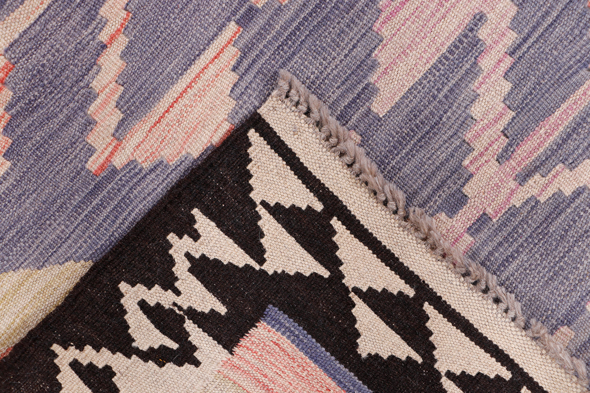 Kilim rug detail with black-and-cream zigzag border and pastel purple triangle motifs.