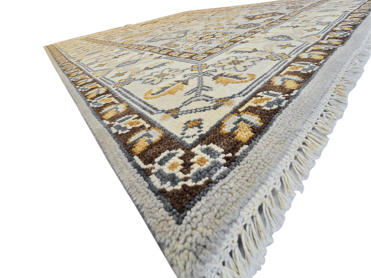 Oushak rug with light ivory pile, dark navy and gold border band, long fringe tassels.