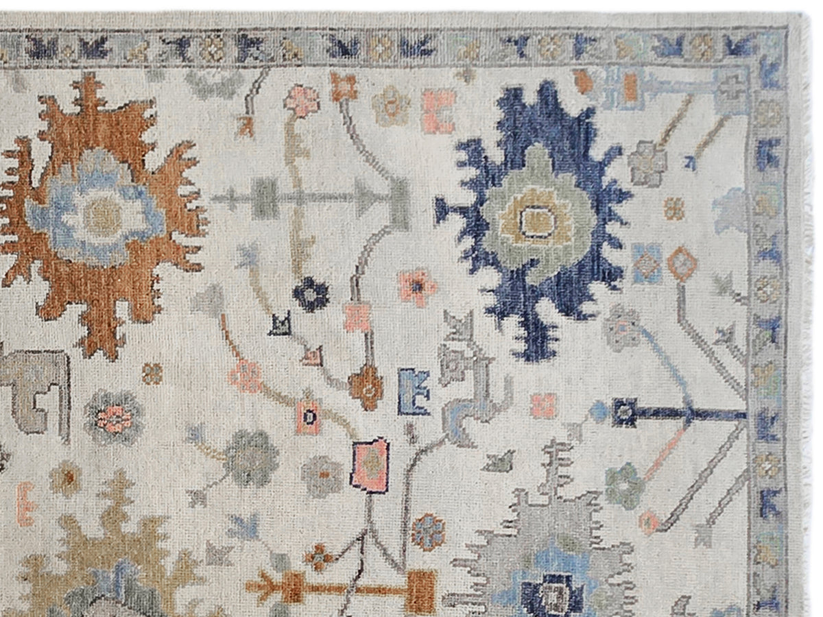 Oushak rug close-up: light background with blue floral medallion and orange geometric accents