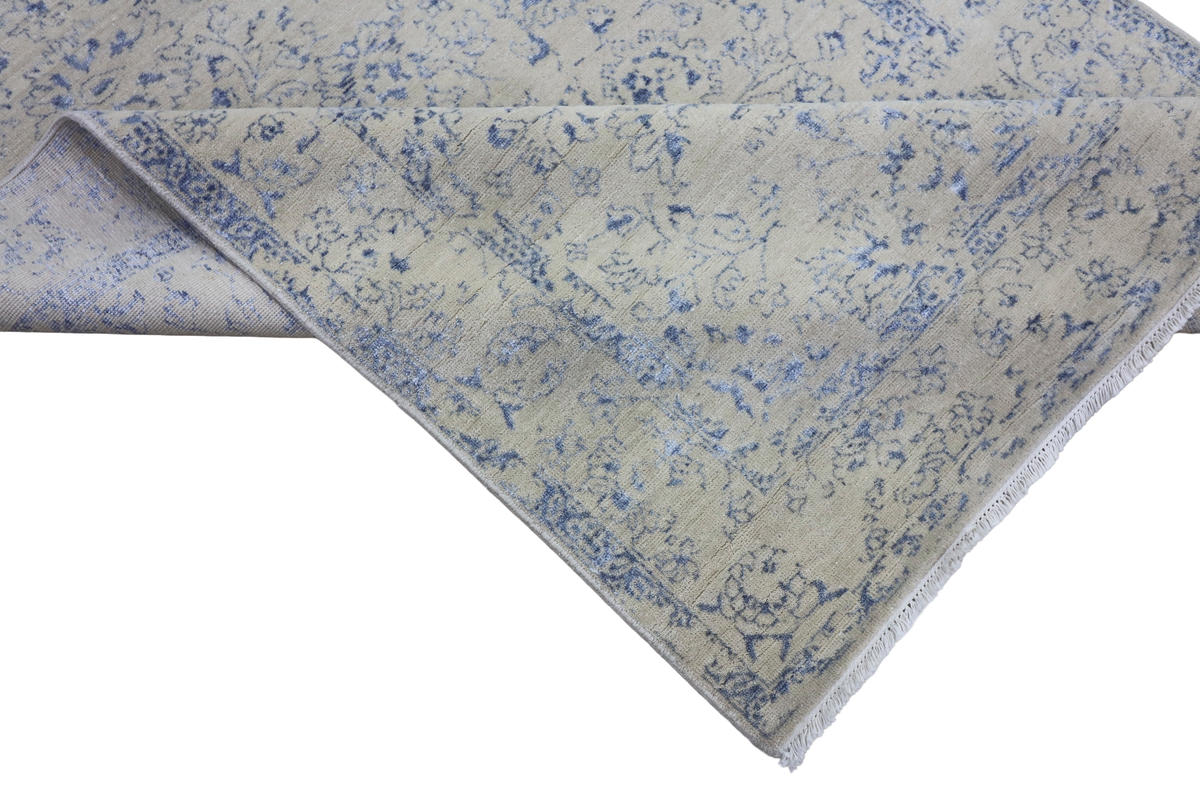 Corner detail of ice blue rug with distressed floral pattern and woven edge