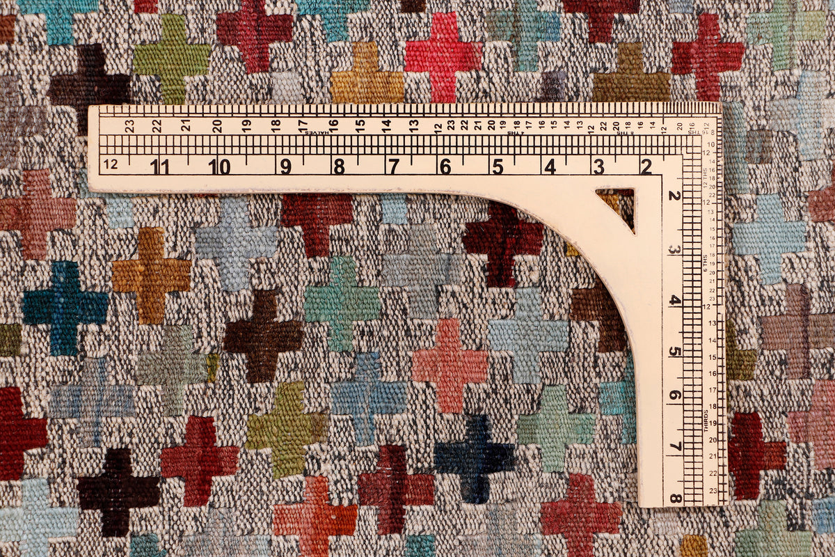Beige kilim rug measuring detail with ruler over multicolor cross pattern.