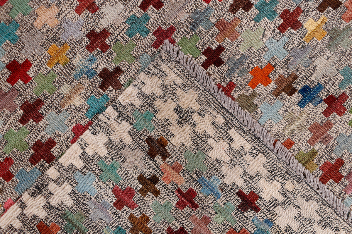 Beige kilim rug corner with multicolor cross motifs and stitched border design.