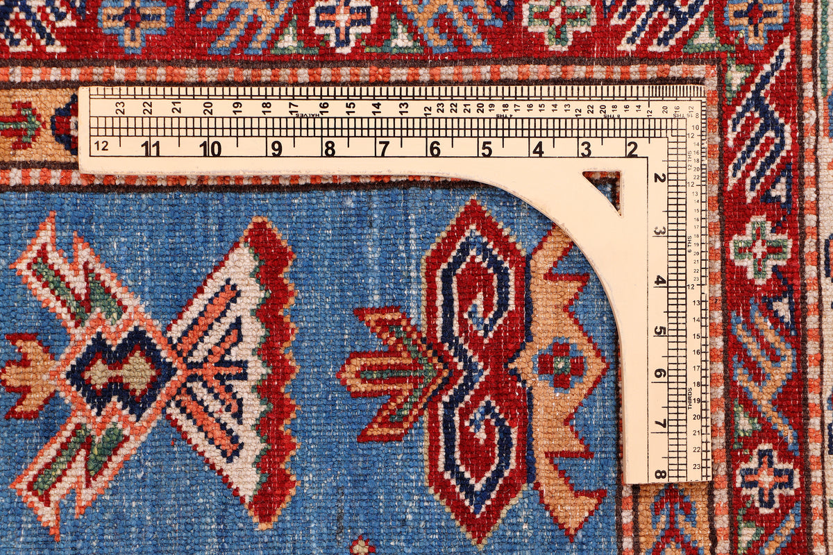 Blue and red Kazak rug edge with ruler measuring width along the border