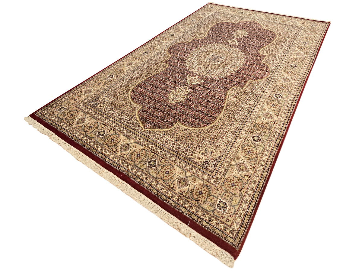 Patterned area rug with dark red and beige floral medallion and cream fringe edge