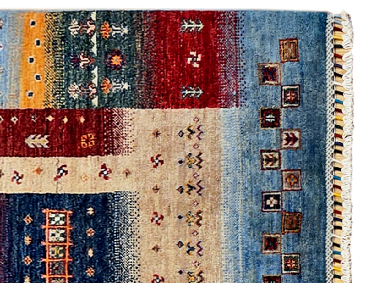 Rug close-up with blue and red panels, small square motifs, cream field, and fringe.