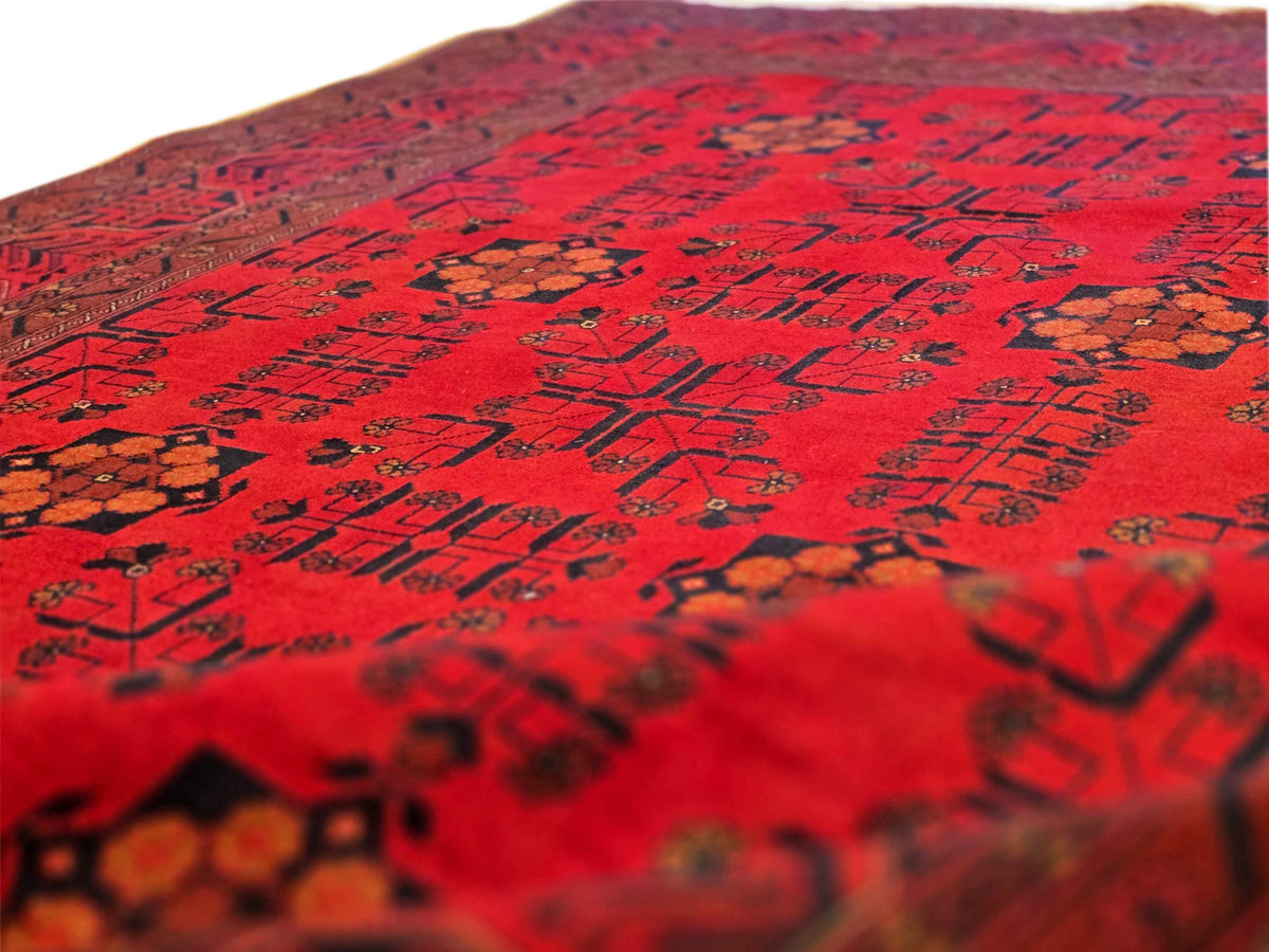 Red rug surface close-up showing dark geometric motifs and warm orange accents.